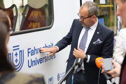 Mężczyzna w okularach i garniturze pokazuje palcem logo Uczelni Fahrenheita umieszczone na tramwaju