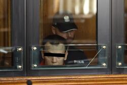 Oskarżony mężczyzna z czarnym paskiem na oczach, za jego plecami siedzi policjant