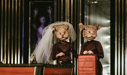 dwoje aktorów stoi na scenie w kostiumach, każde z nich ma na twarzy wielką maskę przedstawiającą głowę szczura