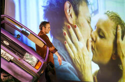 mężczyzna przy przewróconym samochodzie, w tle kadr filmowy, na którym mężczyzna i kobieta się całują