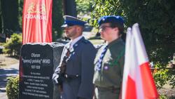 żołnierze stoją przy pomniku z napisem i flagach 