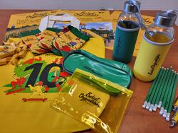 na zdjęciu dwie plastikowe butelki z logo budżetu obywatelskiego, żółte skarpetki w trzech parach, krówki w żółtych papierkach, żółta torba bawełniana i zielone ołówki