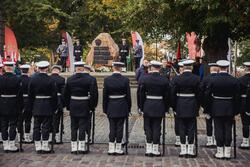 Grupa odwróconych plecami marynarzy stojących przed pomnikiem Polskiego Państwa Podziemnego 