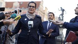 Elegancko ubrana w płaszcz kobieta w okularach wypowiadająca się do dziennikarzy, w tle zabytki Gdańska