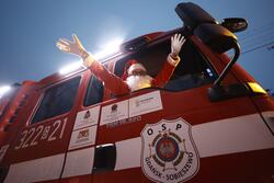 Wóz straży pożarnej (zdjęcie z boku i od dołu), przez okno pasażera wychyla się Mikołaj w czerwonej czapie i rękoma wzniesionymi do góry