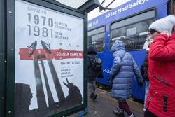 Przystanek tramwajowy na ścianie którego jest plakat informujący o wydarzeniach związanych z rocznicami grudniowymi w Gdańsku. Obok przechodzą ludzie
