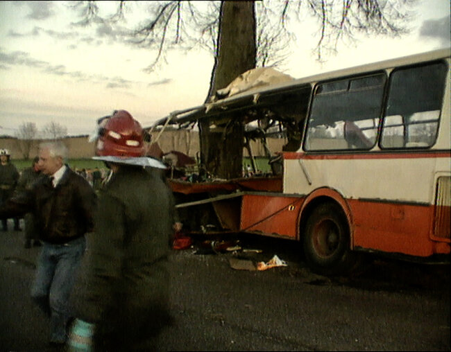 Printscreen z filmu dokumentalnego TVP3 Gdańsk z miejsca katastrofy autobusu w Kokoszkach. Roztrzaskany autobus jest wbity w drzewo, obok chodzą strażacy.