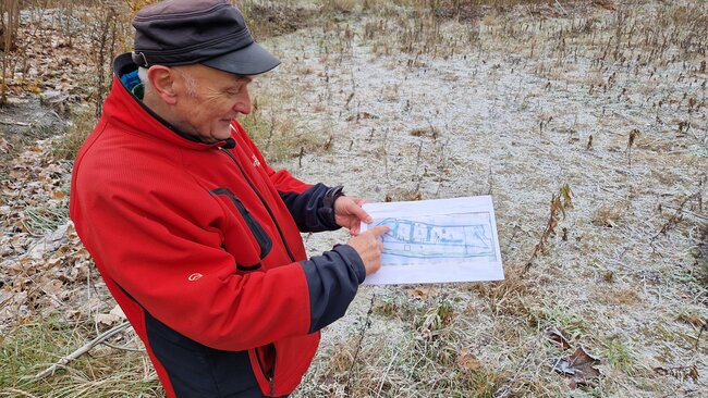 Starszy mężczyzna w czerwonej zimowej kurtce pokazuje palcem na ręcznie wykonaną mapkę terenu