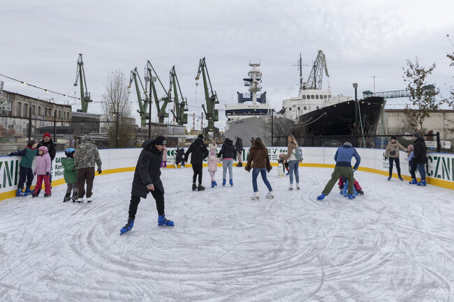 kilka osób jeździ na łyżwach po lodowisku - wokół stoczniowe widoki 