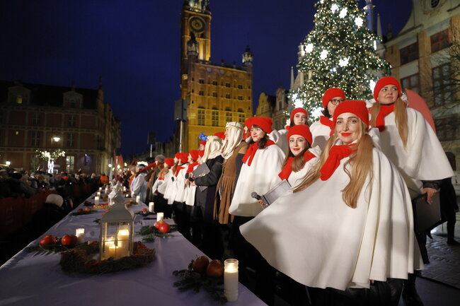 na zdjęciu kilka młodych kobiet w biało czerwonych kostiumach, w tle duża miejska choinka