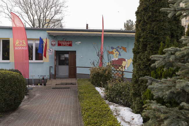 Na zdjęciu widać budynek. Przed wejściem do błękitnego obiektu rozciąga się chodnik z kostki brukowej, a elewację zdobi kolorowy malunek kaczora w kapeluszu. 