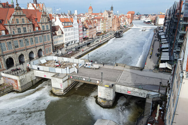 zdjęcie z drona widać zabytkowy most zielony, a na nim ogrodzenie placu robót i koparkę, w tle zabudowa gdańskich kamienic