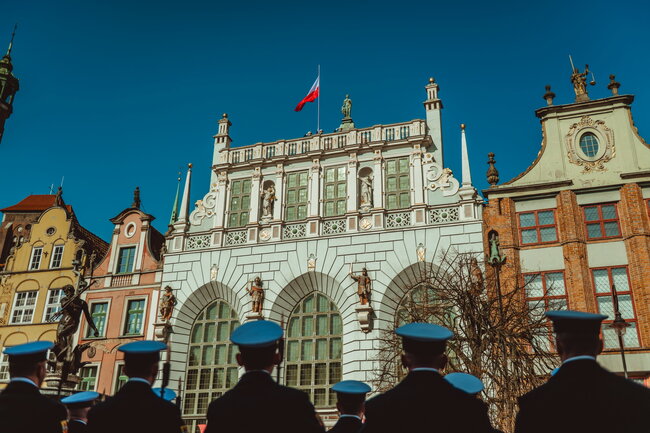 Na renesansowym budynku powiewa polska flaga. Patrzą na to z dołu marynarze marynarki Wojennej.