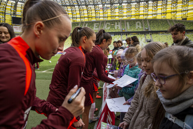 Piłkarki rozdają autografy dzieciom na stadionie.
