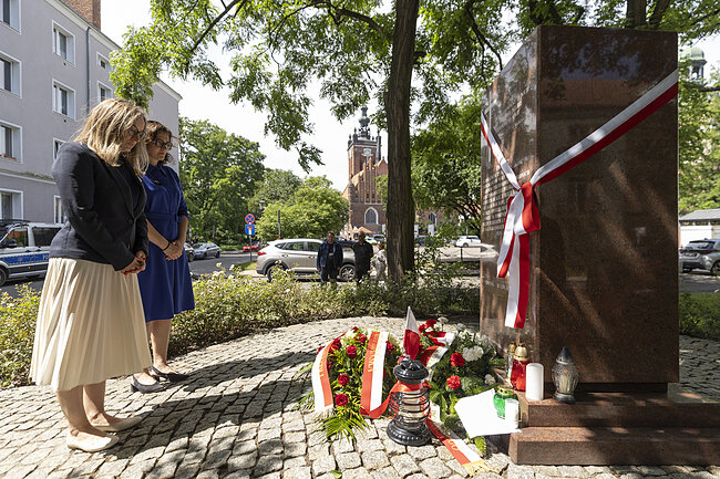 na zdjęciu dwie kobiety po lewej stoją składają hołd ofiarom przy dużym kamiennym pomniku