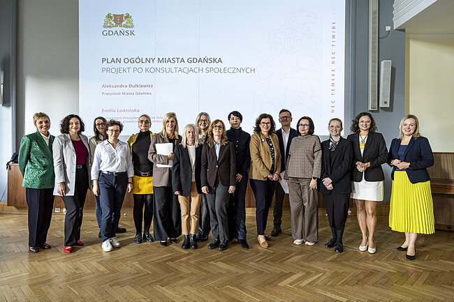 grupa osób na tle ekranu prezentacyjnego z napisem Plan ogólny miasta gdańska. projekt po konsutacjach