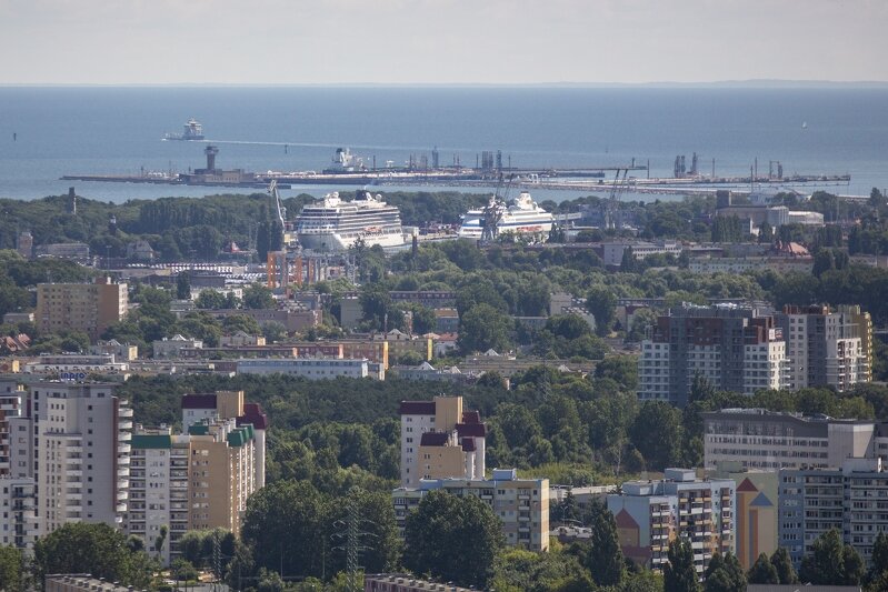 Na zdjęciu panorama Gdańska, widać bloki mieszkaniowe, drzewa zielone, a także fragment Zatoki Gdańskiej