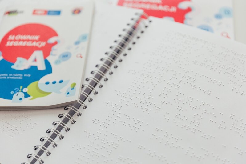 Otwarta książeczka, białe kartki na nim dziurki (pismo w systemie Braille’a) 