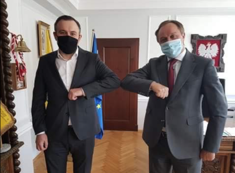 Dwóch mężczyzn w ciemnych garniturach styka się łokciami