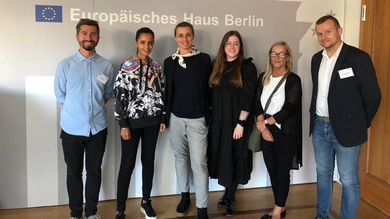 Sześć uśmiechniętych osób stoi pod ścianą. Na ścianie napis i logo Unii Europejskiej