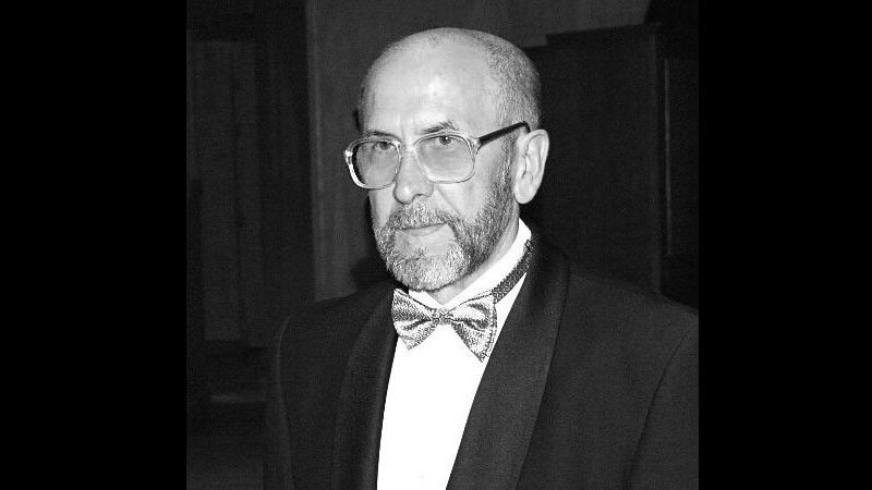 Czarno-białe zdjęcie: twarz starszego mężczyzny w okularach pod muchą