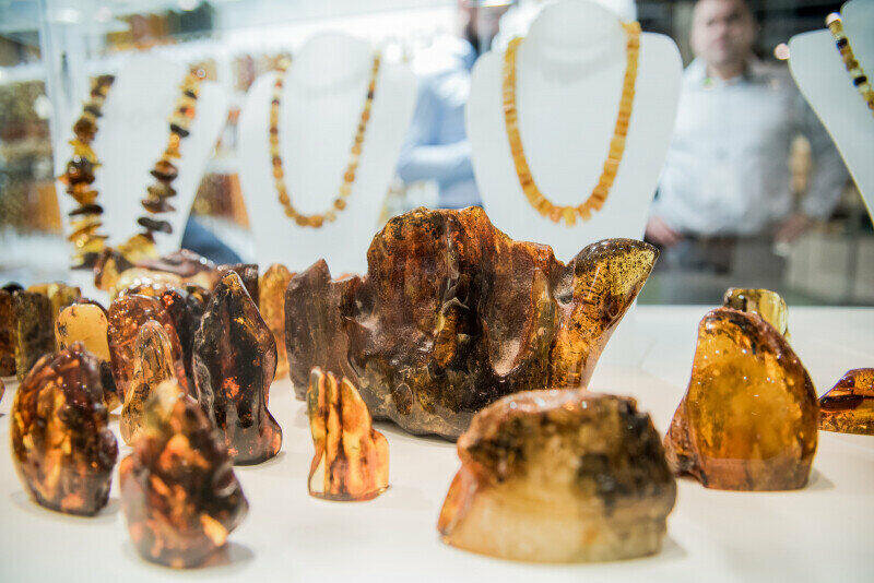bursztynowe bryły wyeksponowane na stanowisku, w tle bursztynowe naszyjniki