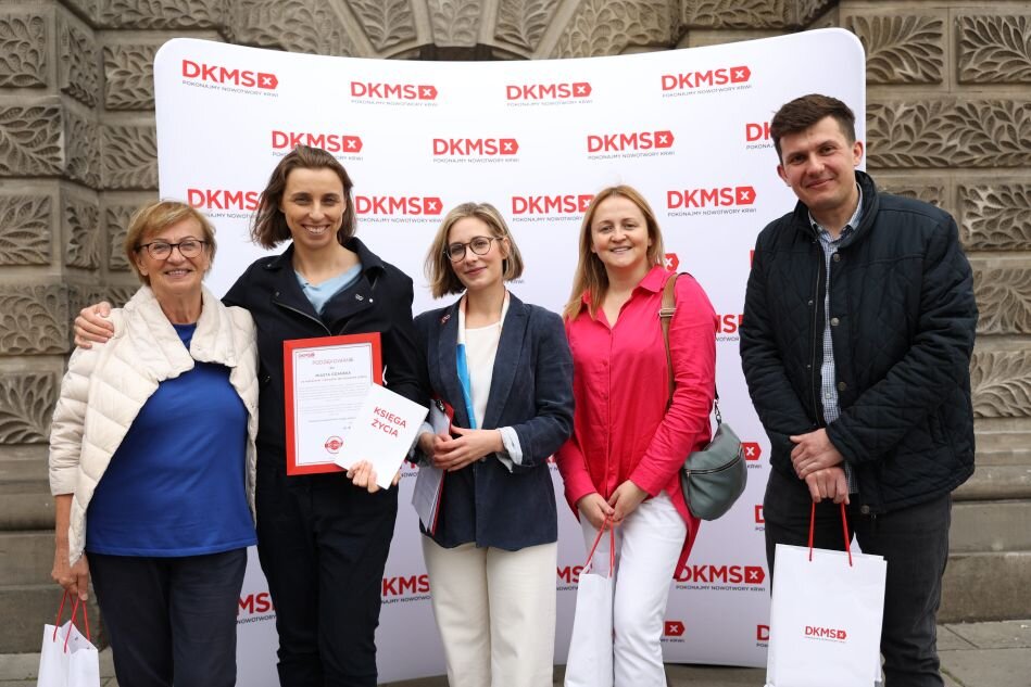 grupa kobiet i mężczyzn na tle zabytkowej fasady i plakatu Fundacji DKMS