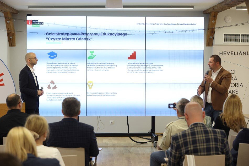 Sala, ekran, na krzesłach siedzi kilka osób w różnym wieku i patrzy w ekran 