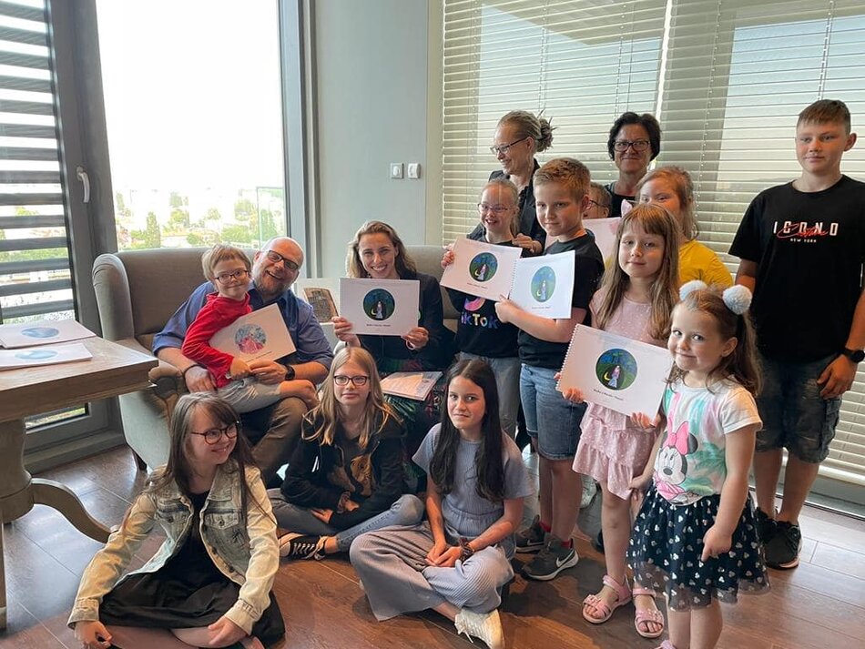 Grupa dzieci z pracami plastycznymi, efektami zajęć, warsztatów siedzi lub stoi w kręgu