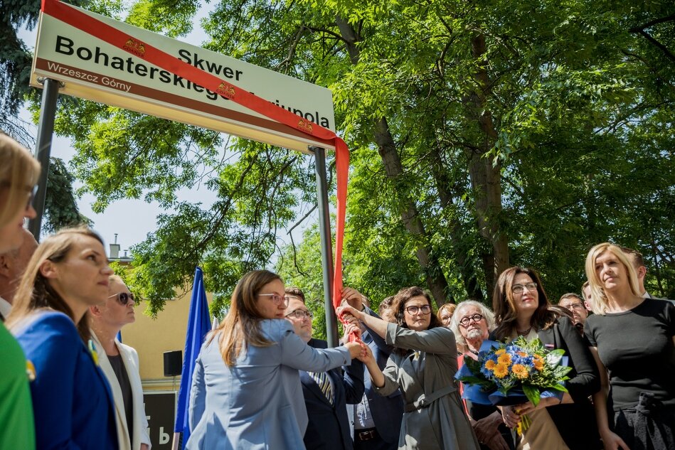 grupa osób pod tablicą z napisem Skwer Bohaterskiego Mariupola, szarfę czerwoną ściągają z niej dwie kobiety i jeden mężczyzna