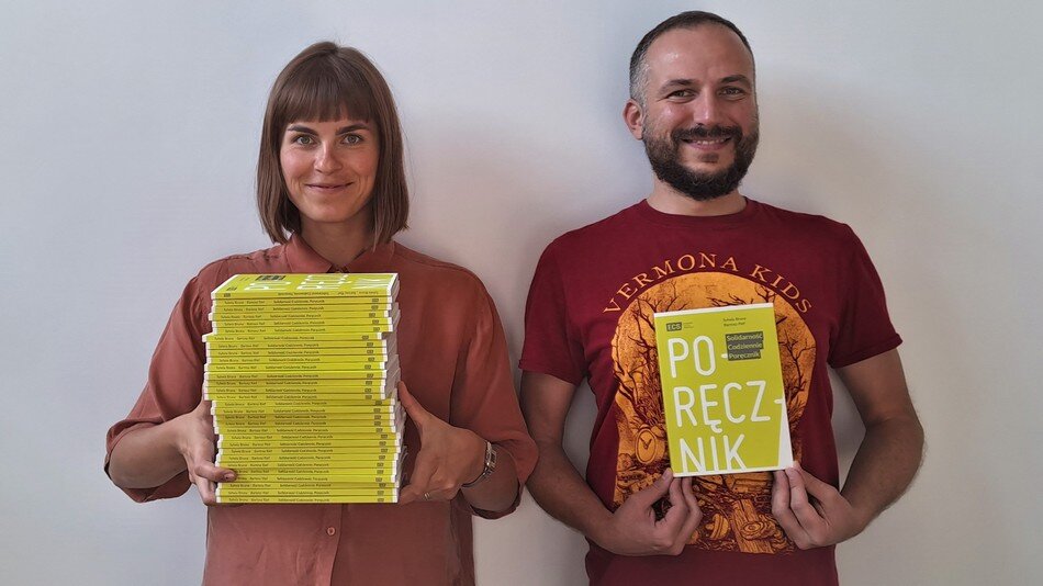 Kobieta i mężczyzna w koszulkach trzymają książki. Po lewej kobieta stos, po prawej mężczyzna pokazuje okładkę z napisem PODRĘCZNIK 