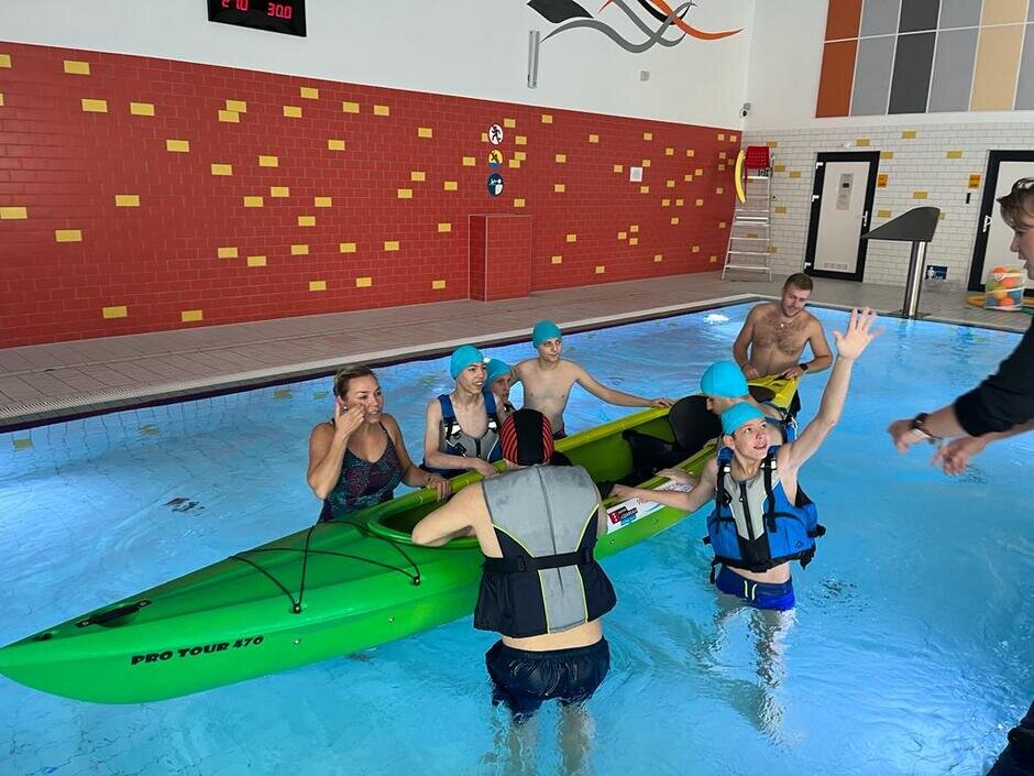 zapoznanie ze sprzętem wodnym - uczniowie szkoły podstawowej wsiadają do kajaka podczas zajęć prowadzonych w basenie