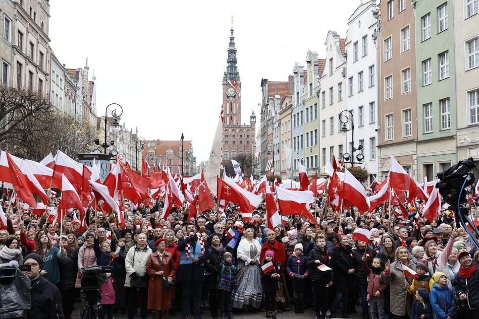 na zdjęciu grupa kilkuset osób z których większość trzyma flagi polski i gdańska, po prawej i lewej stronie widać fragmenty gdańskich kamienic, w tle zabytkowy budynek ratusza