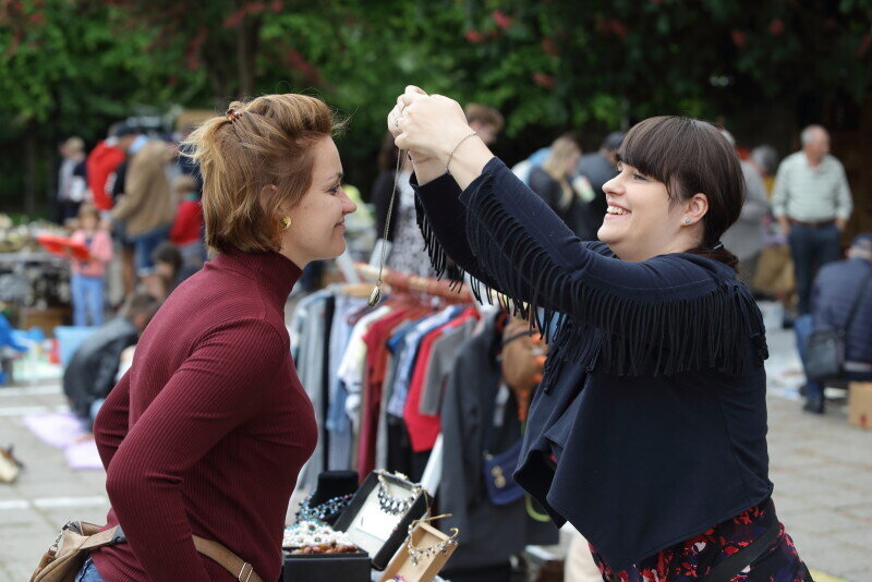 Dwie kobiety na targu. Po prawej zakłada naszyjnik na szyję tej po lewej 