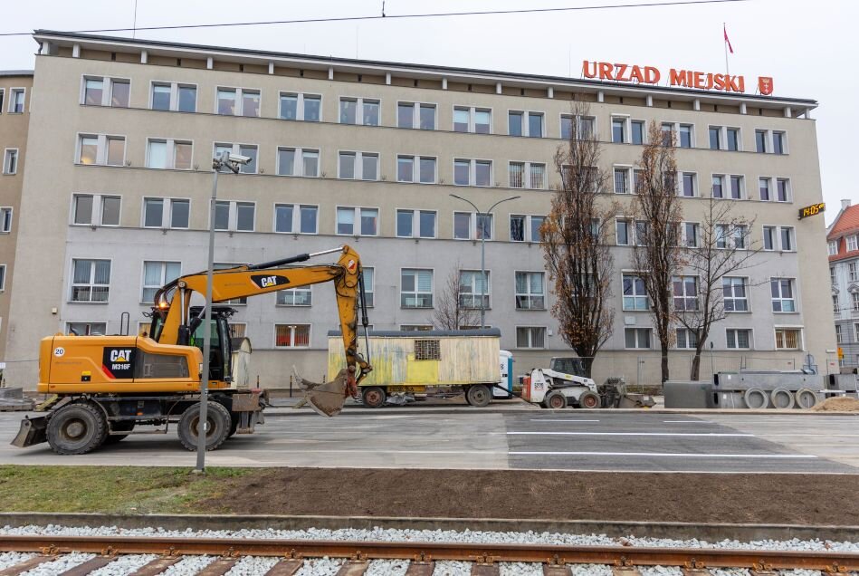 koparka jedzie po ulicy, obok barierki