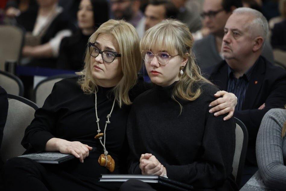 dwie kobiety ubrane na czarno, w okularach, siedzą przytulone do siebie, na kolanach mają książki