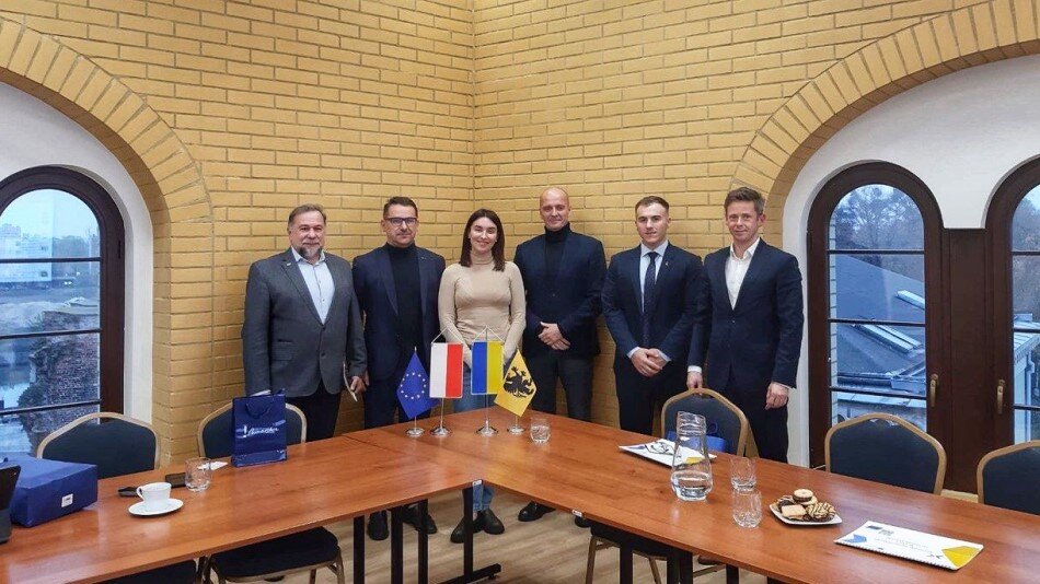 Kilka osób stojących w uroczystych pozach przy stole, na której stoją m.in. flagi Polski i Ukrainy 