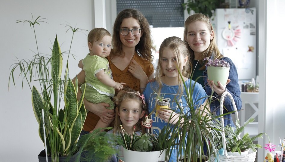 wymieniona kobieta i jej córki w wieku od 10 miesięcy do 14 lat pozują przed stołem z doniczkami z roślinnością