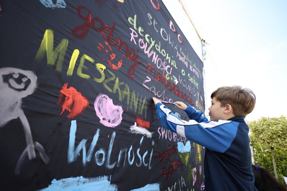 mały chłopiec pisze na czarnej ścianie pełnej haseł np. wolności, mieszkania, solidarności ...