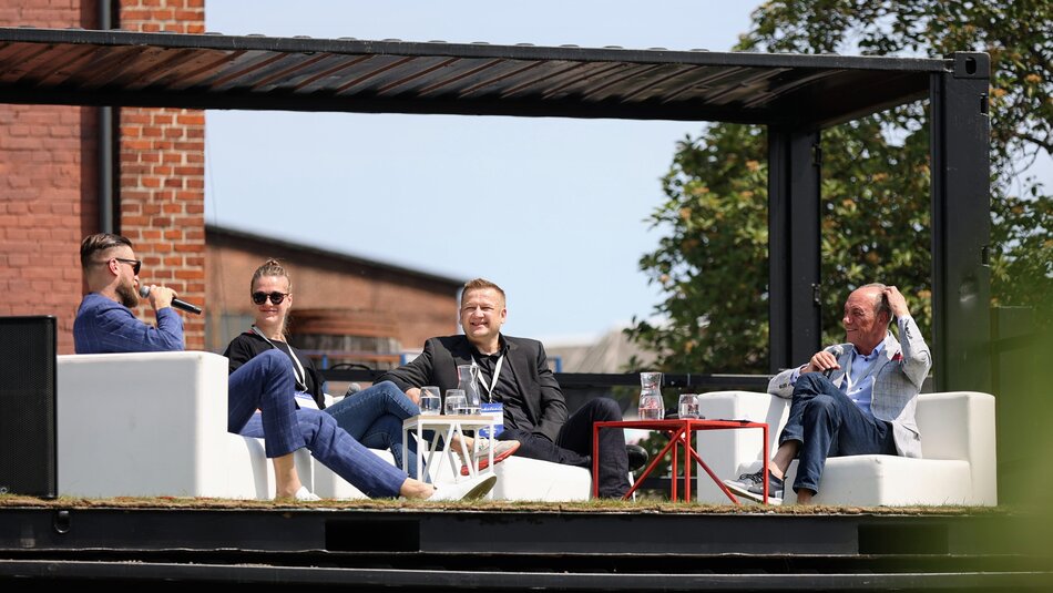 Kilka osób siedzących przy stoliku pod gołym niebem i dyskutujących ze sobą