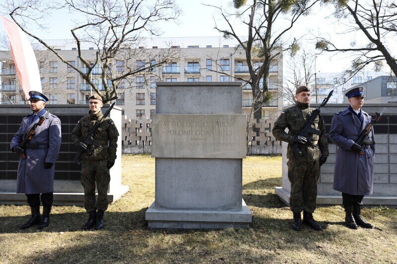 Pomnik w kształcie prostokąta z napisem W hołdzie ofiarom - Polonii Gdańskiej. Po bokach po dwóch żołnierzy w galowych mundurach z bronią