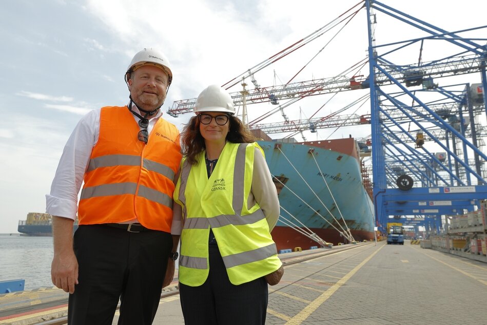 Kobieta i mężczyzna stoją na nabrzeżu na tle wielkiego kontenerowca, suwnic i innych urządzeń portowych