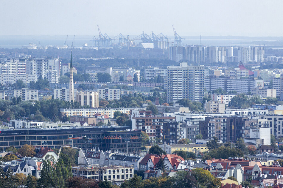 szeroka panorama miasta, na pierwszym planie nowoczesne budynki biurowe, za nimi bloki, kościół, w tle widoczne portowe dźwigi i morze