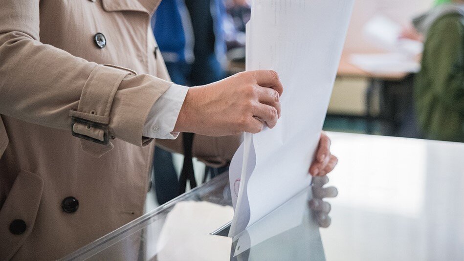 Osoba w płaszczu wrzucająca kartę do głosowania do urny