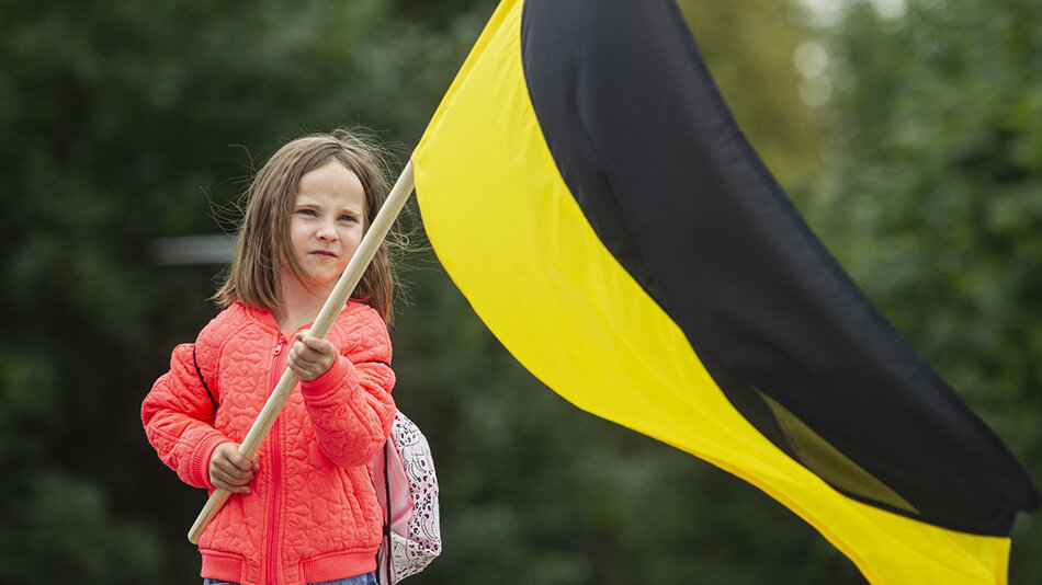 kilkuletnia dziewczynka trzyma w ręku czarno-żółtą flagę