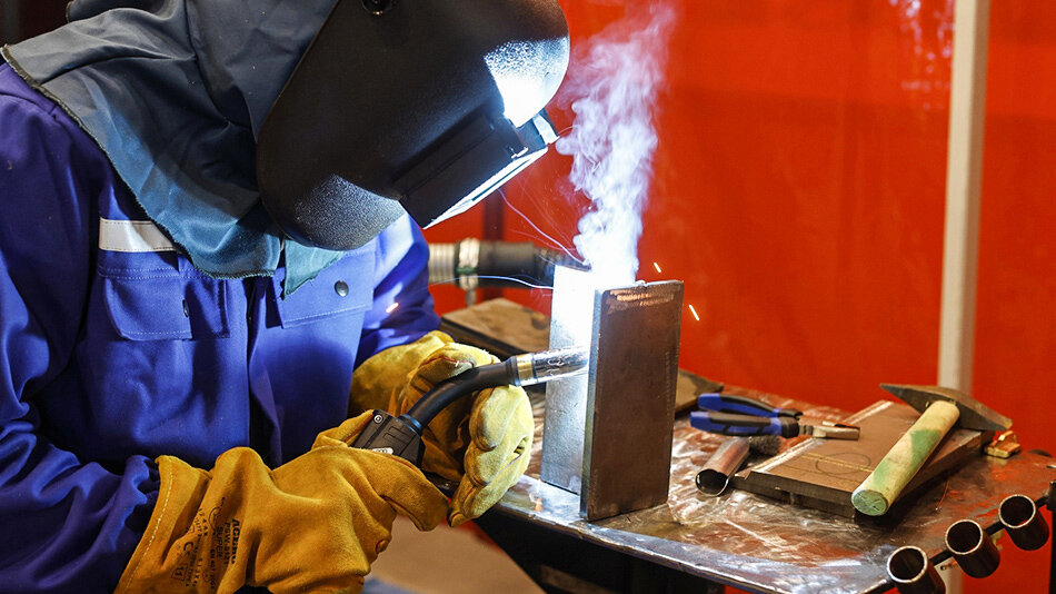 człowiek w kombinezonie i masce na twarzy spawa ze sobą metalowe elementy