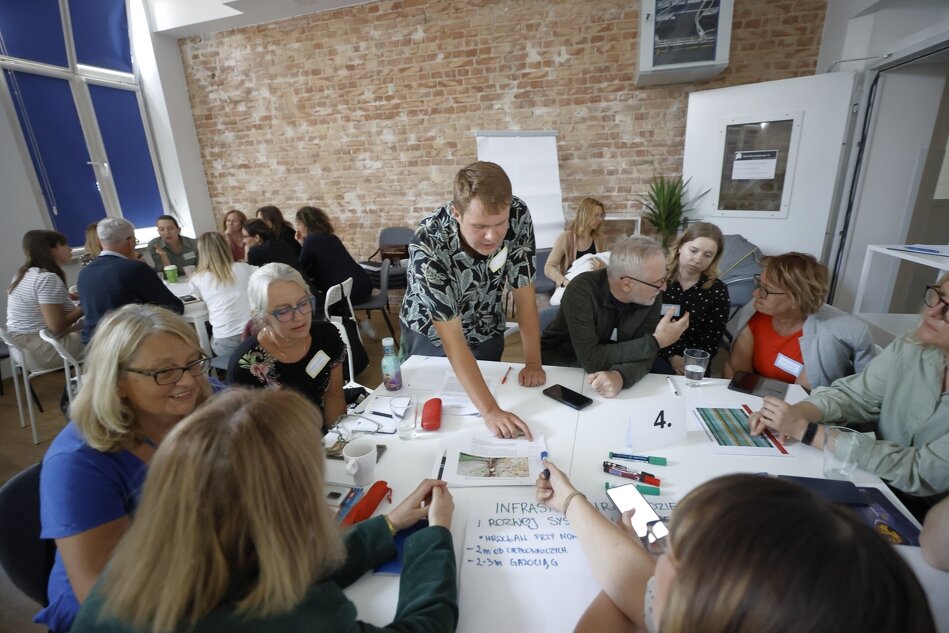 Grupa ludzi siedzi przy stole, na którym leżą różne dokumenty