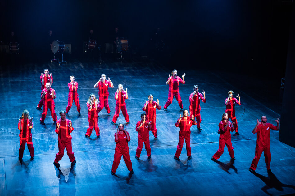 kilkudziesięciu tancerzy w czerwonych kombinezonach na scenie