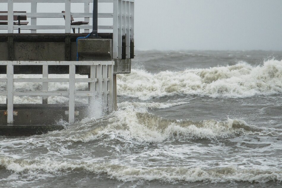 Na zdjęciu wzburzone morze, po lewej stronie zdjęcia biały pomost, na którym stoi ławka