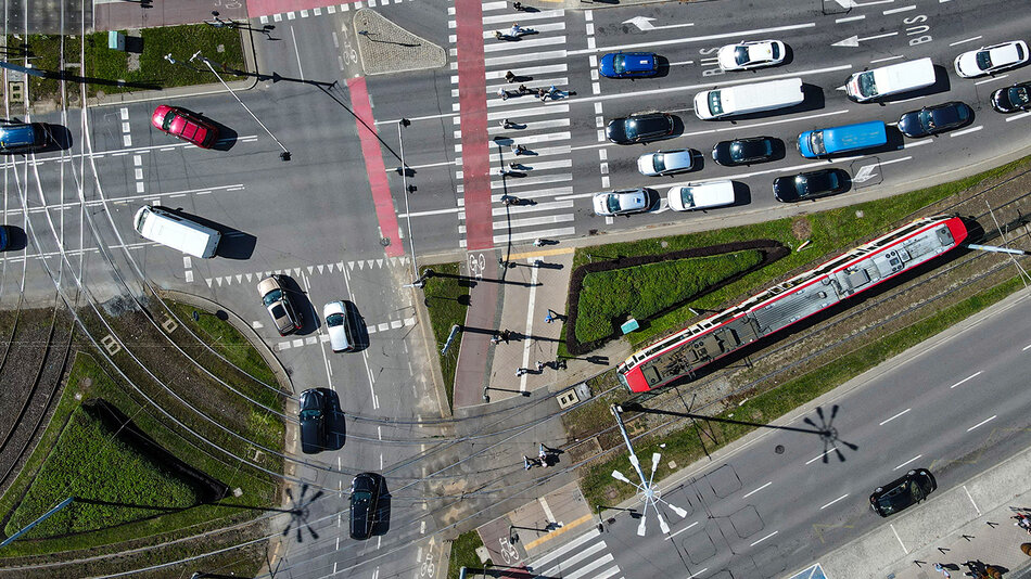 skrzyżowanie wielopasmowych jezdni na których poruszają się samochody z przejściami dla pieszych i torami tramwajowymi widziane z lotu ptaka